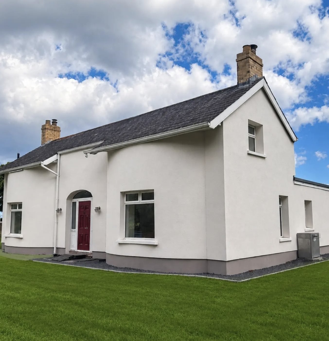 Detached cottage in a white finish with curved walls, a grey plinth and a red door