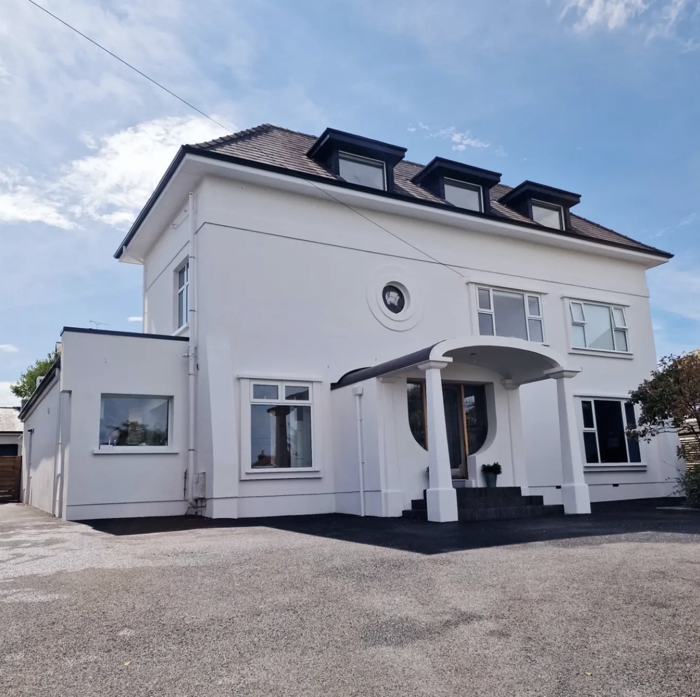 Large detached house in a white finish with a curved entrance canopy and three dormers