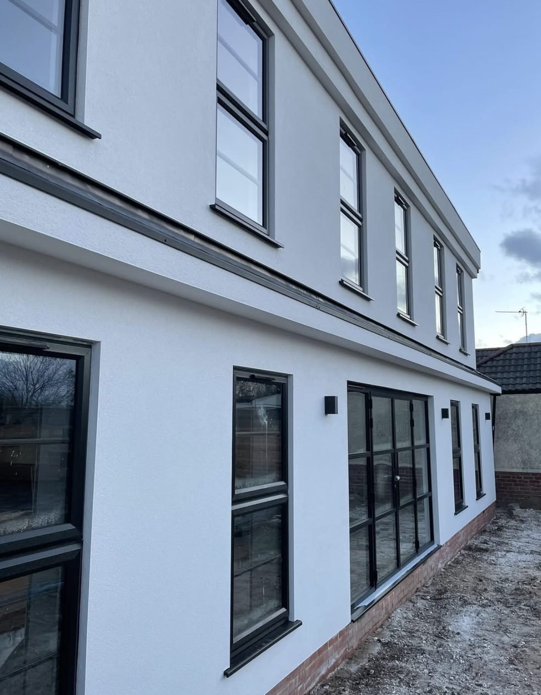 Long two-storey side wall in white with a dark band and black windows