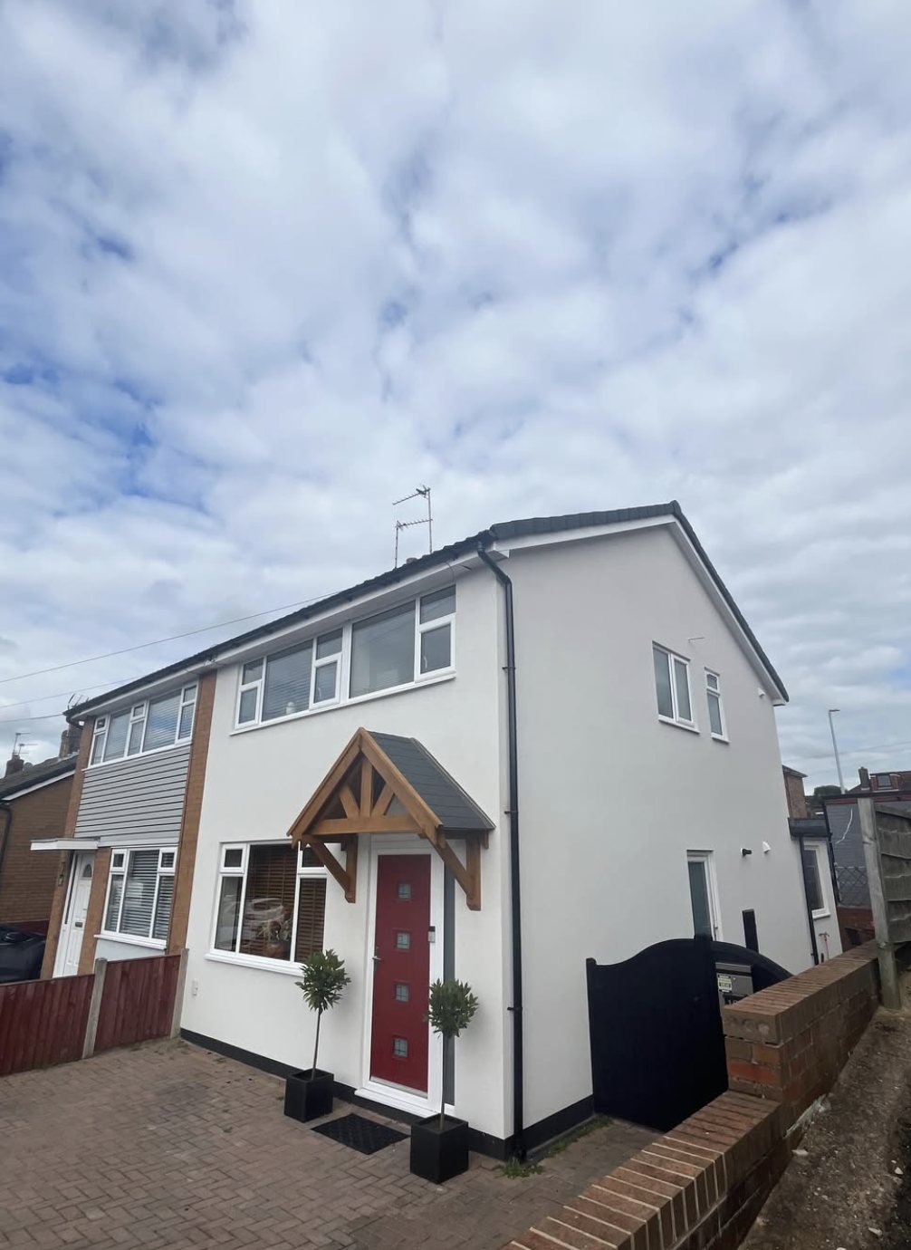 Semi-detached house finished in white with an oak porch, red front door and dark plinth