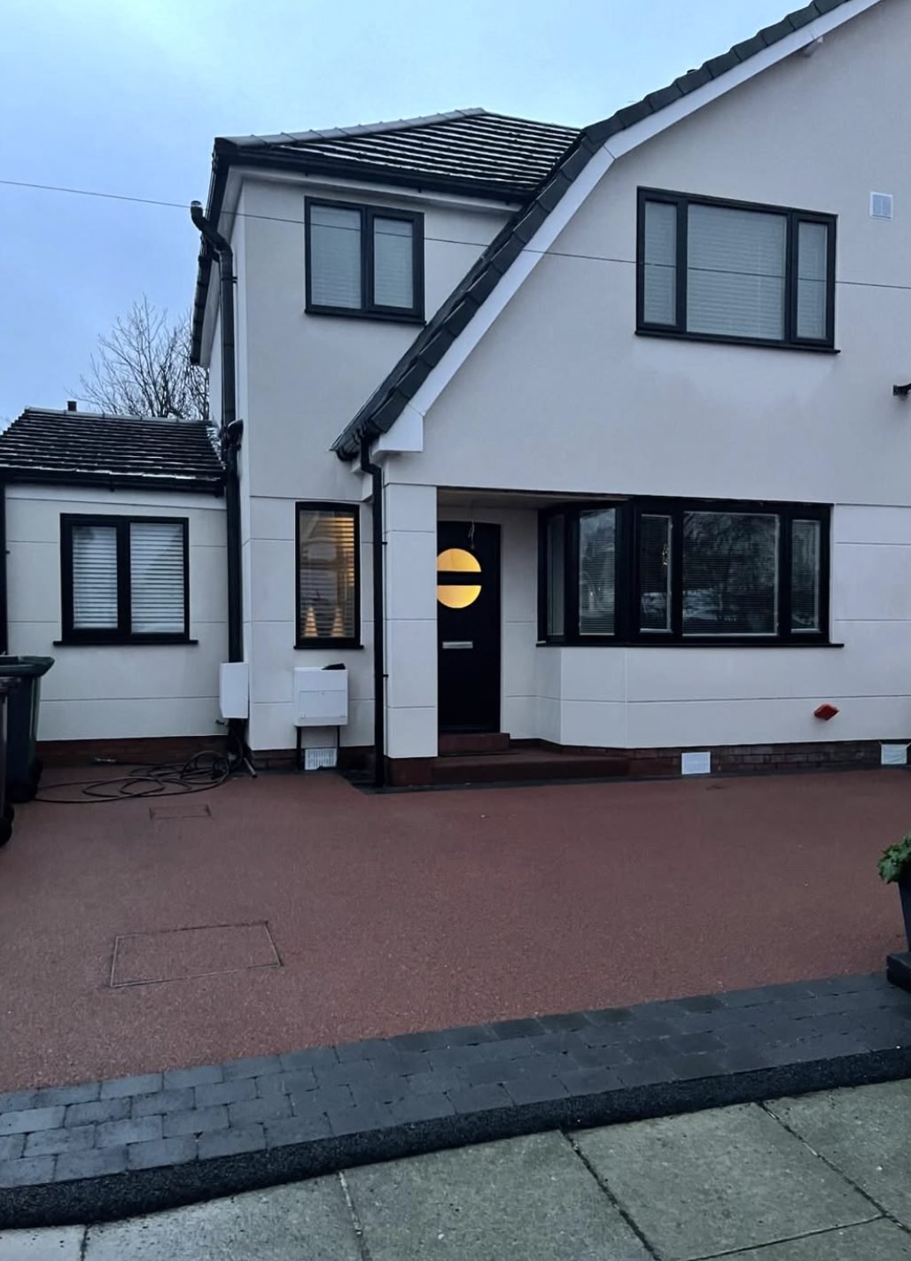 House in white with dark window frames and a red paved drive